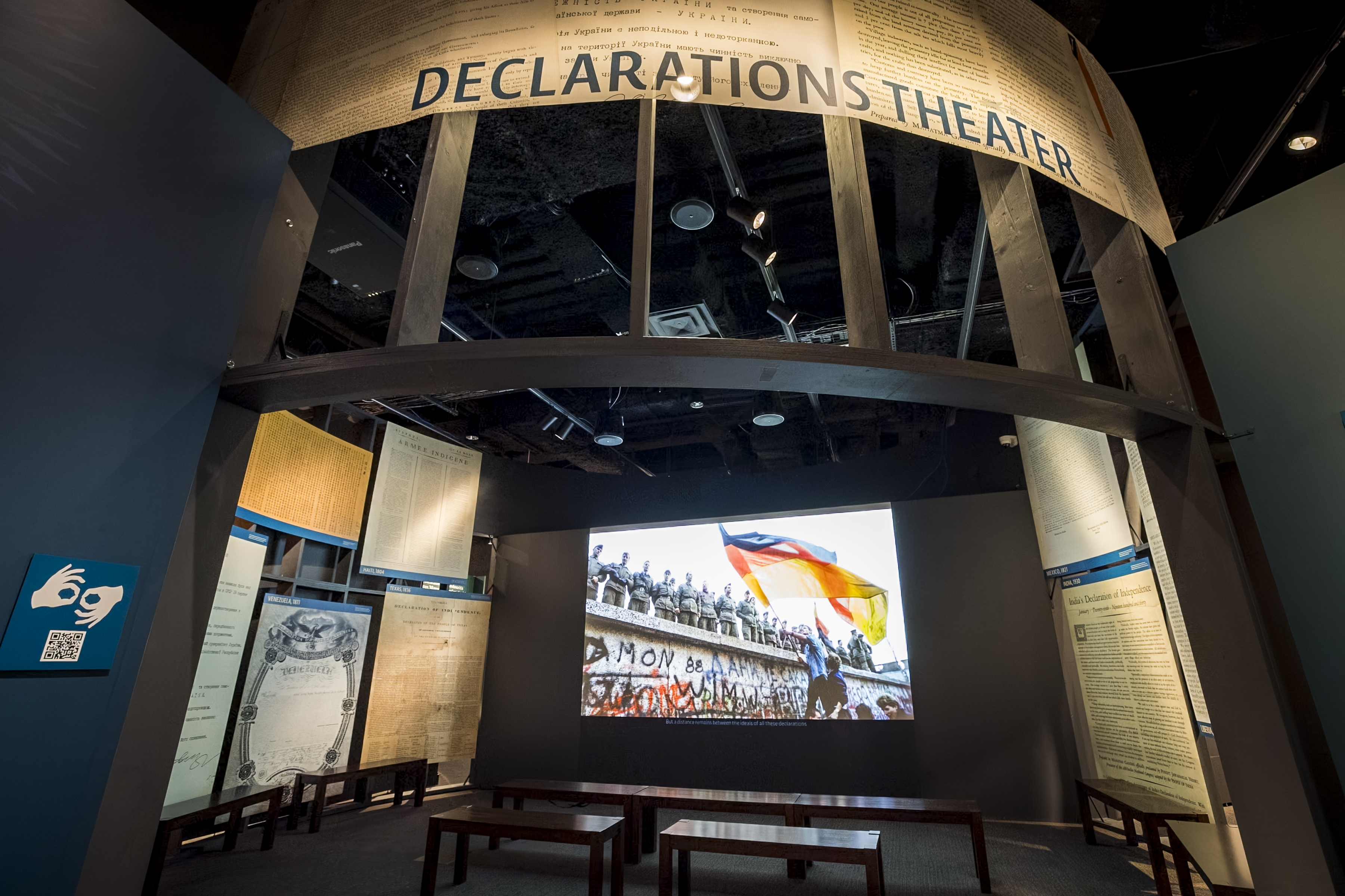 A screen surrounded by large reproductions of documents. A sign above says Declarations Theater and an ASL symbol with a QR code is on the wall to the left