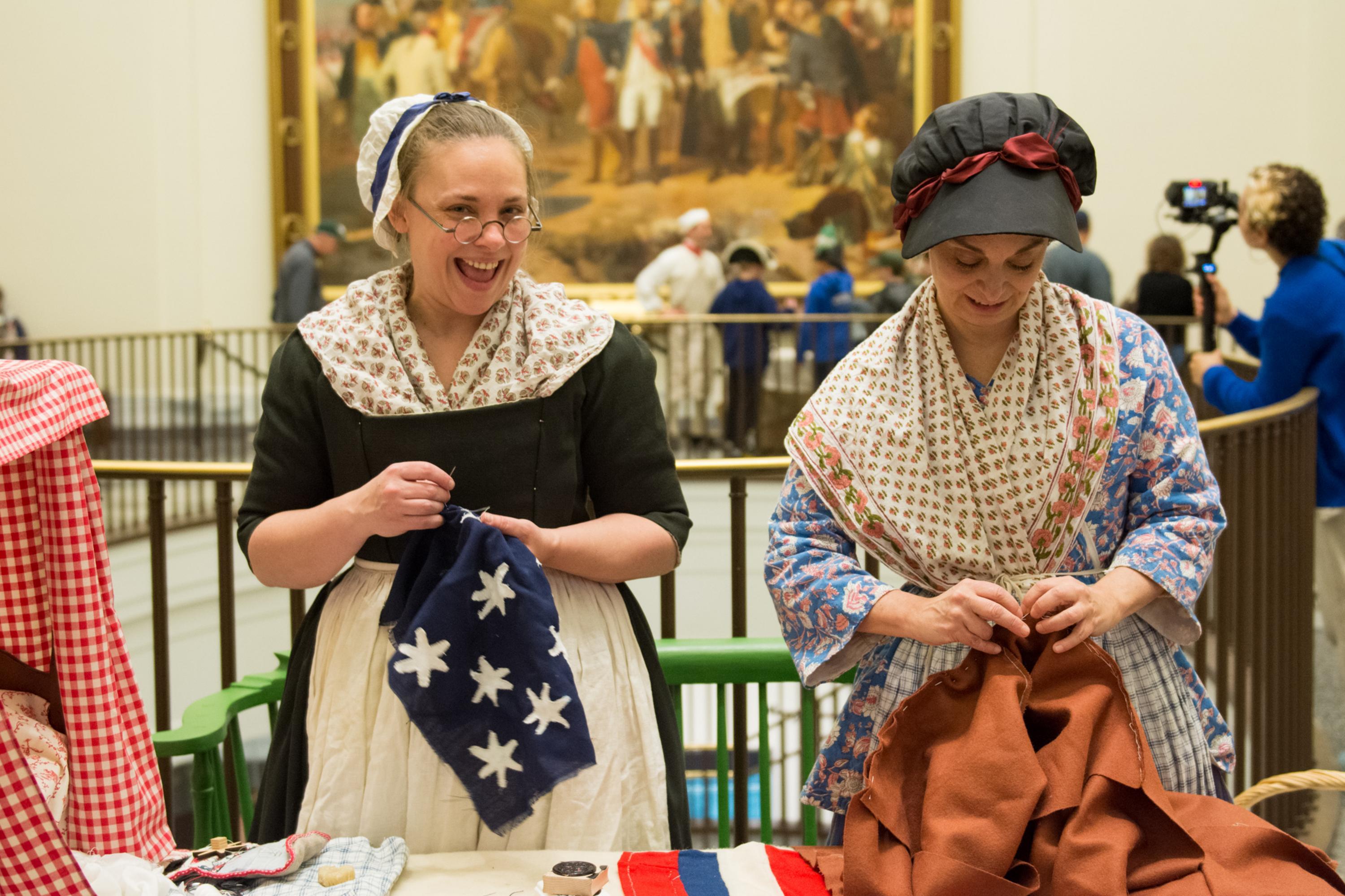 Two costumed interpreters sew inside the Museum