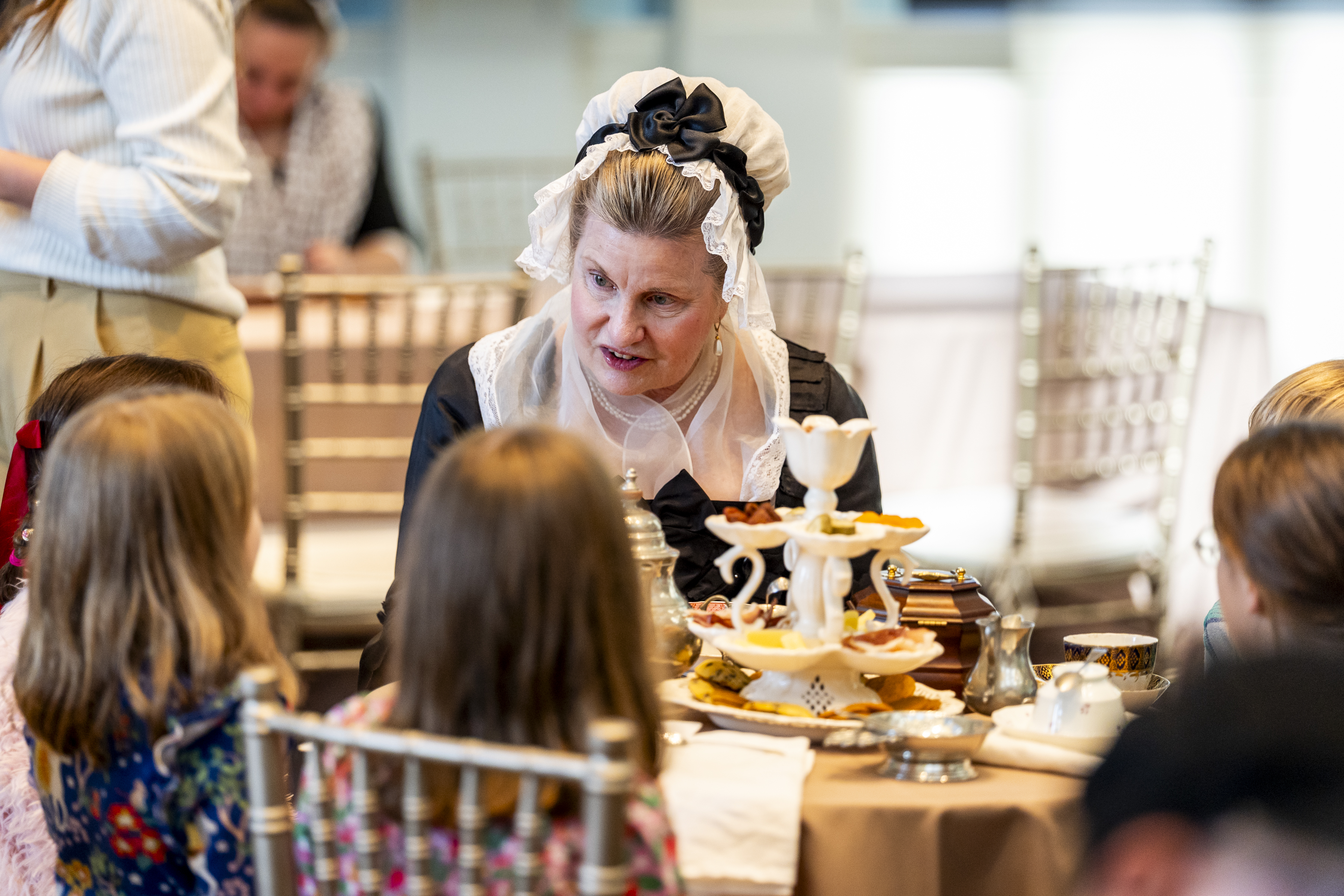 A group of children sit at a table with a costumed interpreter