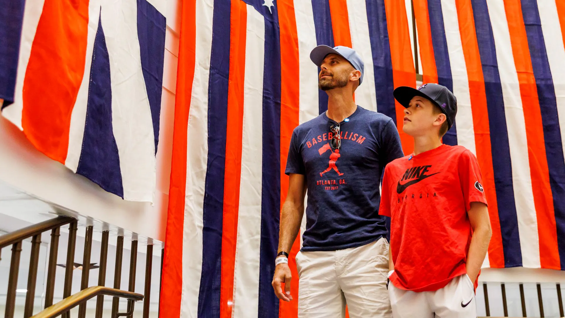 A man and child stand in front of hanging red, white, and blue striped flags