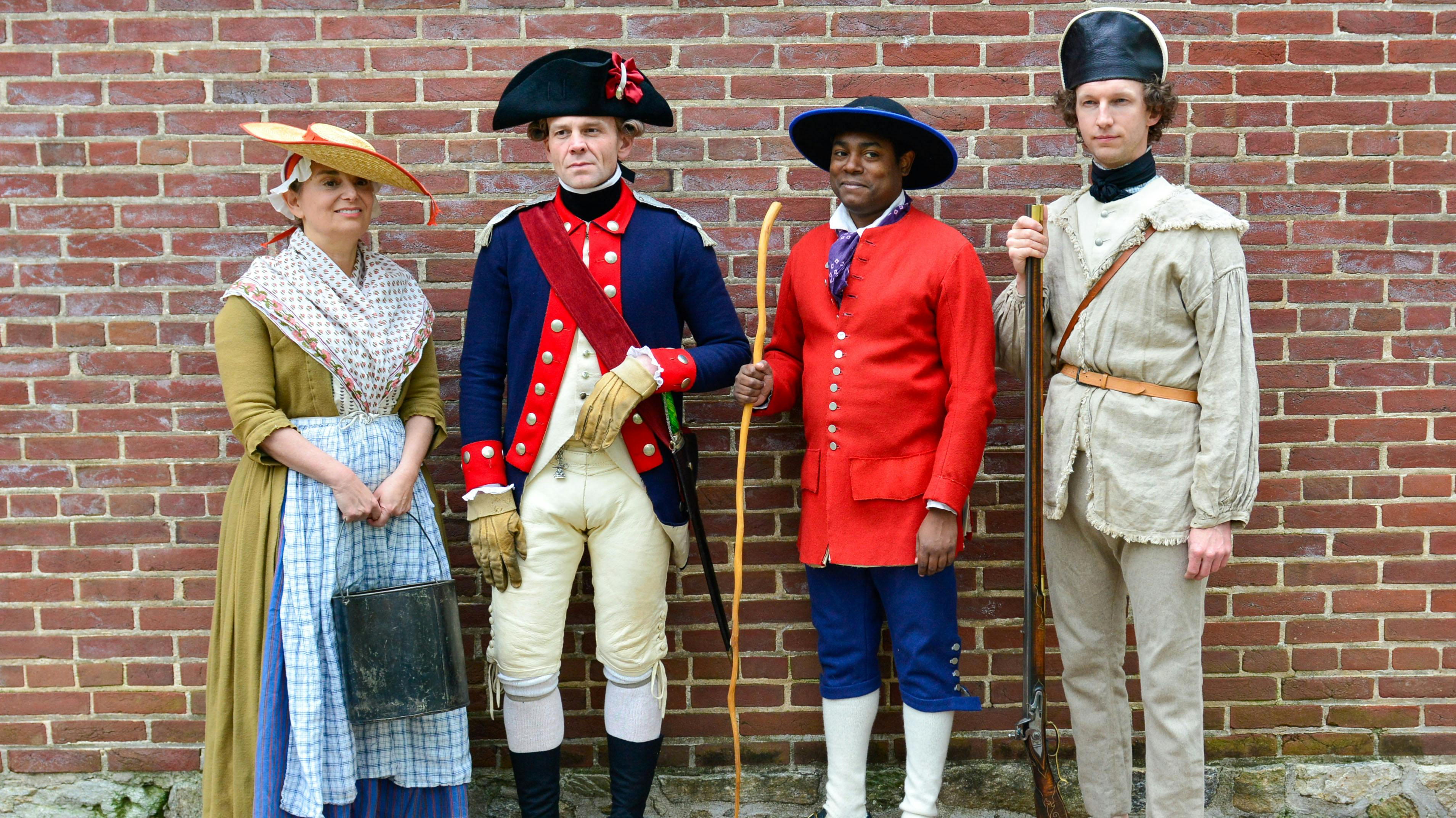 Four costumed living historians stand in front a brick wall in Independence National Historical Park.