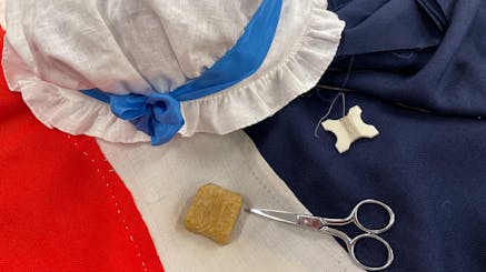 image of red, which, and blue fabric, a white bonnet, scissors, thread, and other flag making tools.