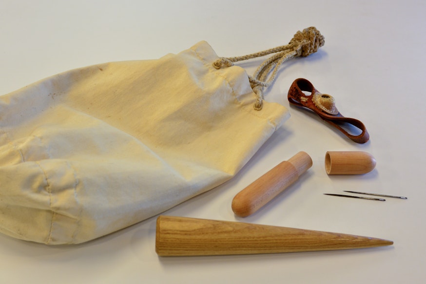 A canvas ditty bag with a fid, sewing needles, and a thimble.