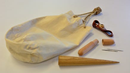 A canvas ditty bag with a fid, sewing needles, and a thimble.