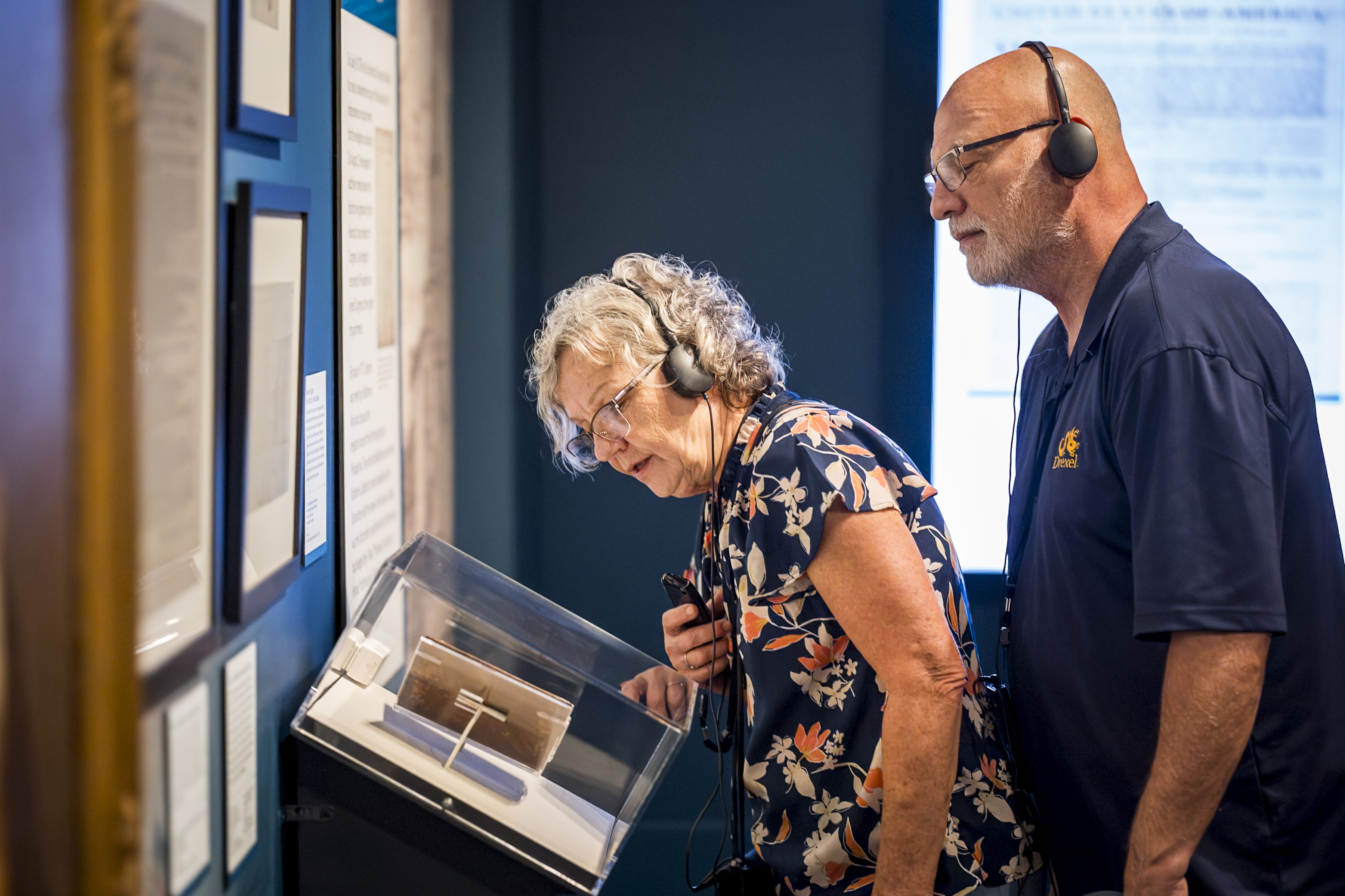 Two people wearing headphones look into a glass case in "The Declaration's Journey" exhibition