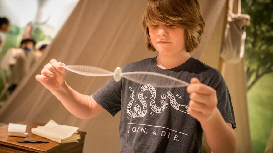 A white adolescent male plays with a Revolutionary-style whirligig.
