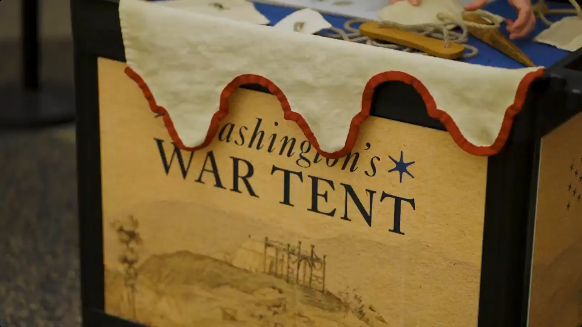 The side of a cart with the words Washington's War Tent, and a red and white cloth draped over it