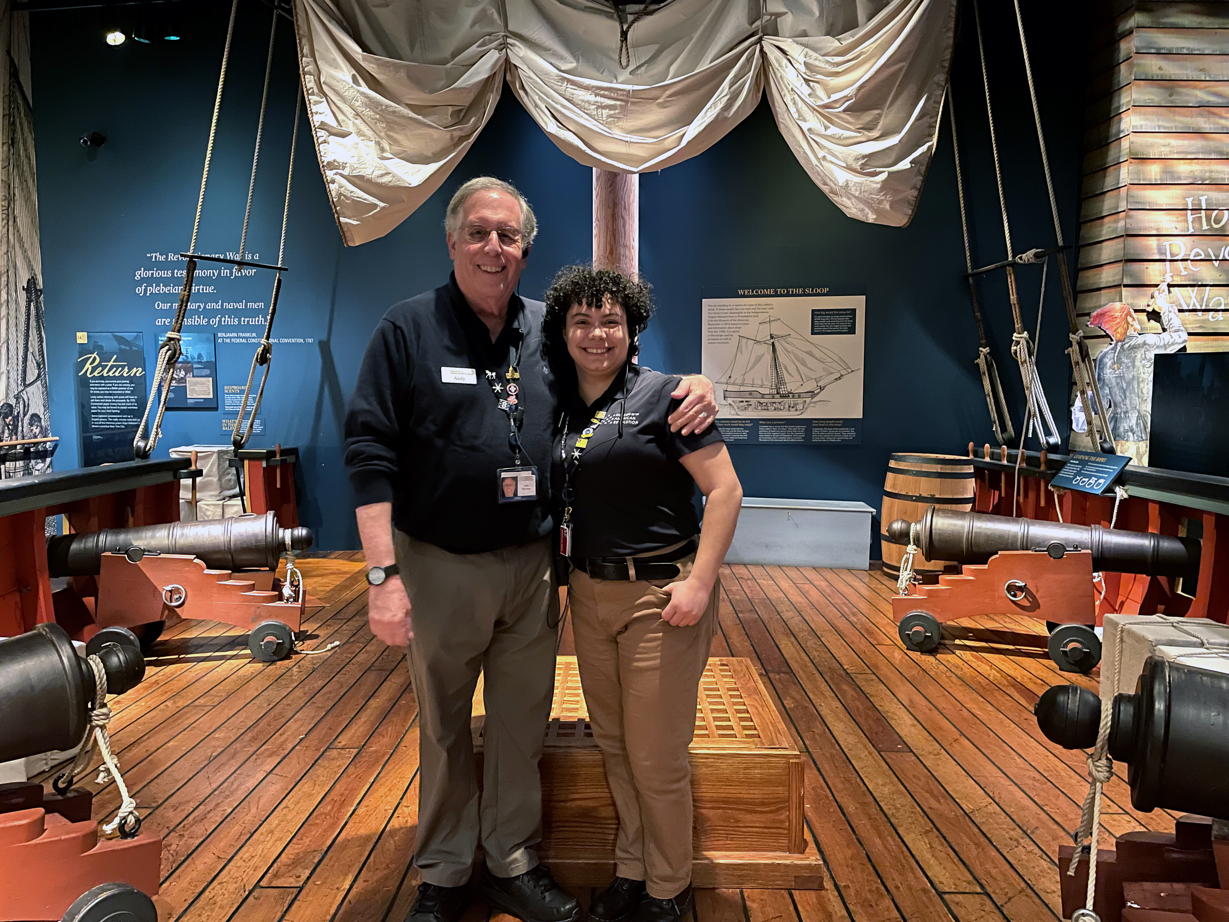 Two people in uniform stand on the replica ship in the Museum's galleries
