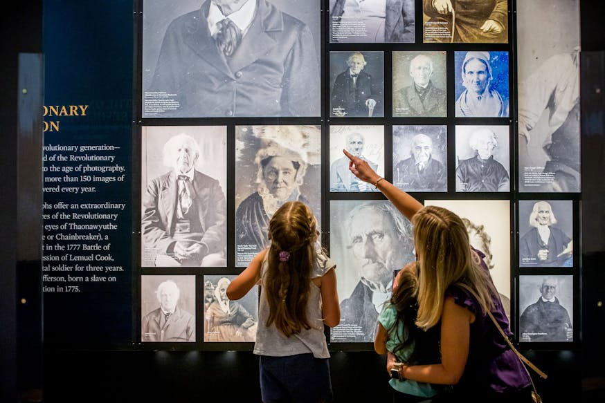 A mother and two young daughters look at photos on the Revolutionary Generation Wall at the Museum.