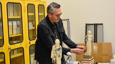 Artist John Wind who is wearing a black jacket, dark jeans, and glasses, works on one of his Whiskey Rebellion decanters in the Museum's collections workroom.