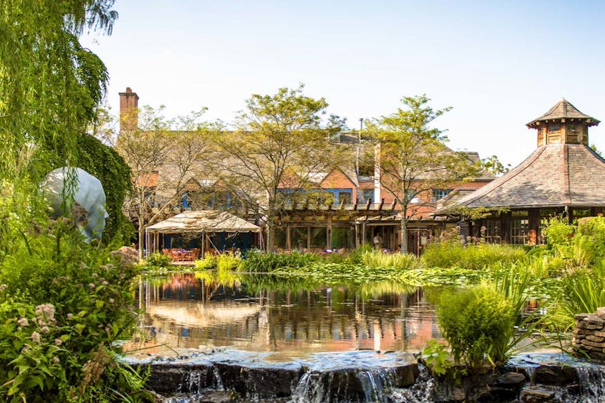 This image shows a pond, greenery, and wooden building that's part of Grounds for Sculpture in New Jersey.