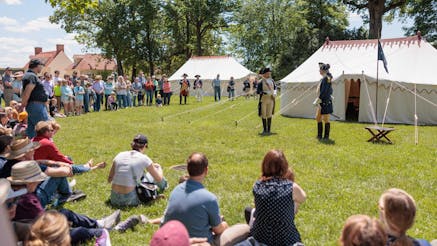 A crowd watches costumed historical interpreters on Mount Vernon's green lawn in front of the Museum's replicas of George Washington's tents.