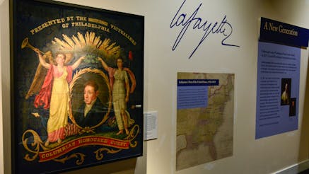 A painted silk parade banner featuring a portrait of the Marquis de Lafayette displayed in the Witness to Revolution exhibit.