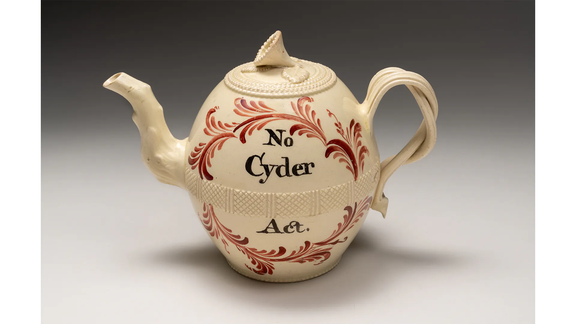 A cream-colored teapot with a red design and the text No Cyder Act