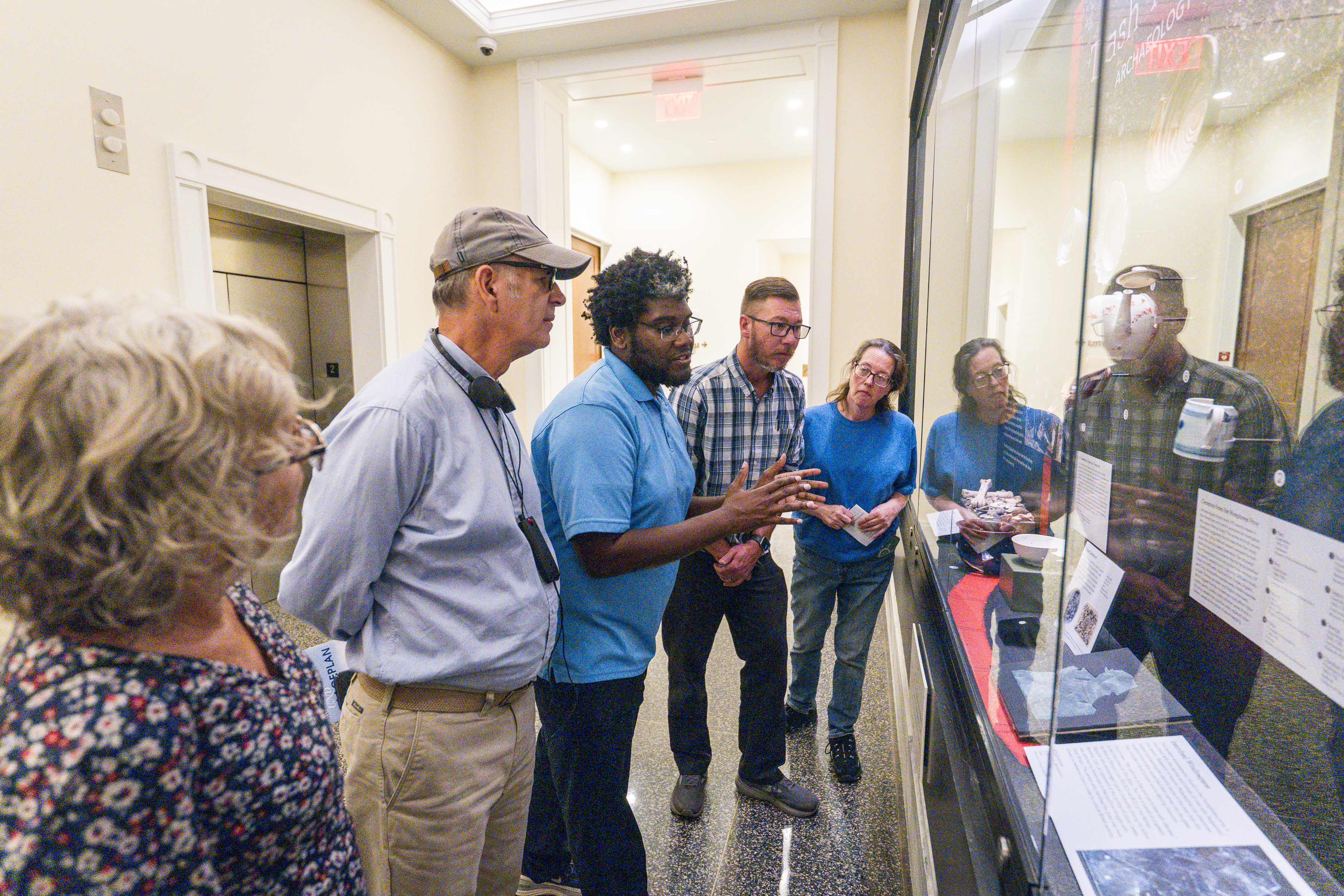 A tour guide speaks to a group of adults in front of a glass case