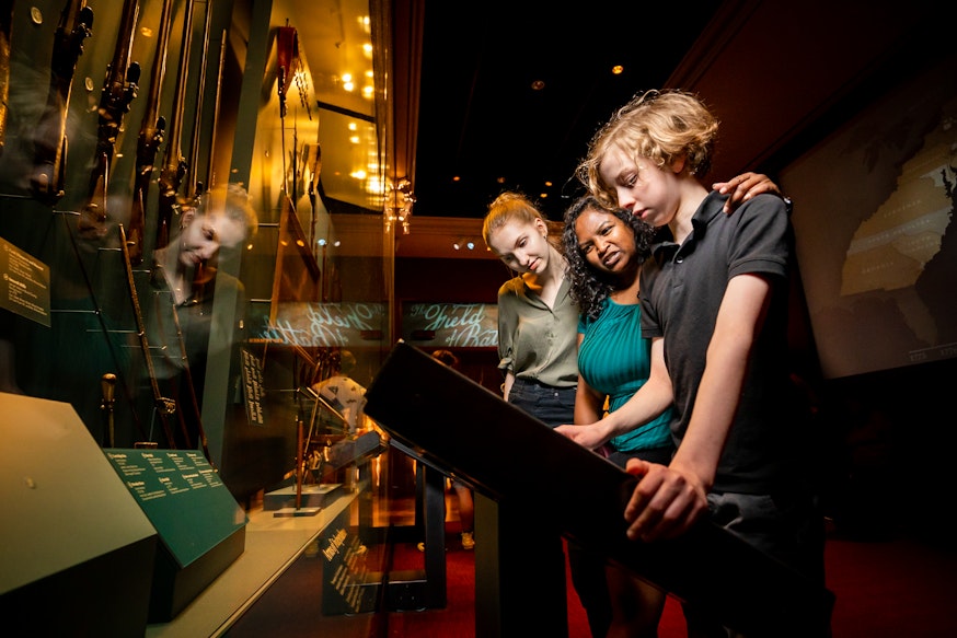 Three guests view the Arms of Independence case and touch screen in the Museum galleries.