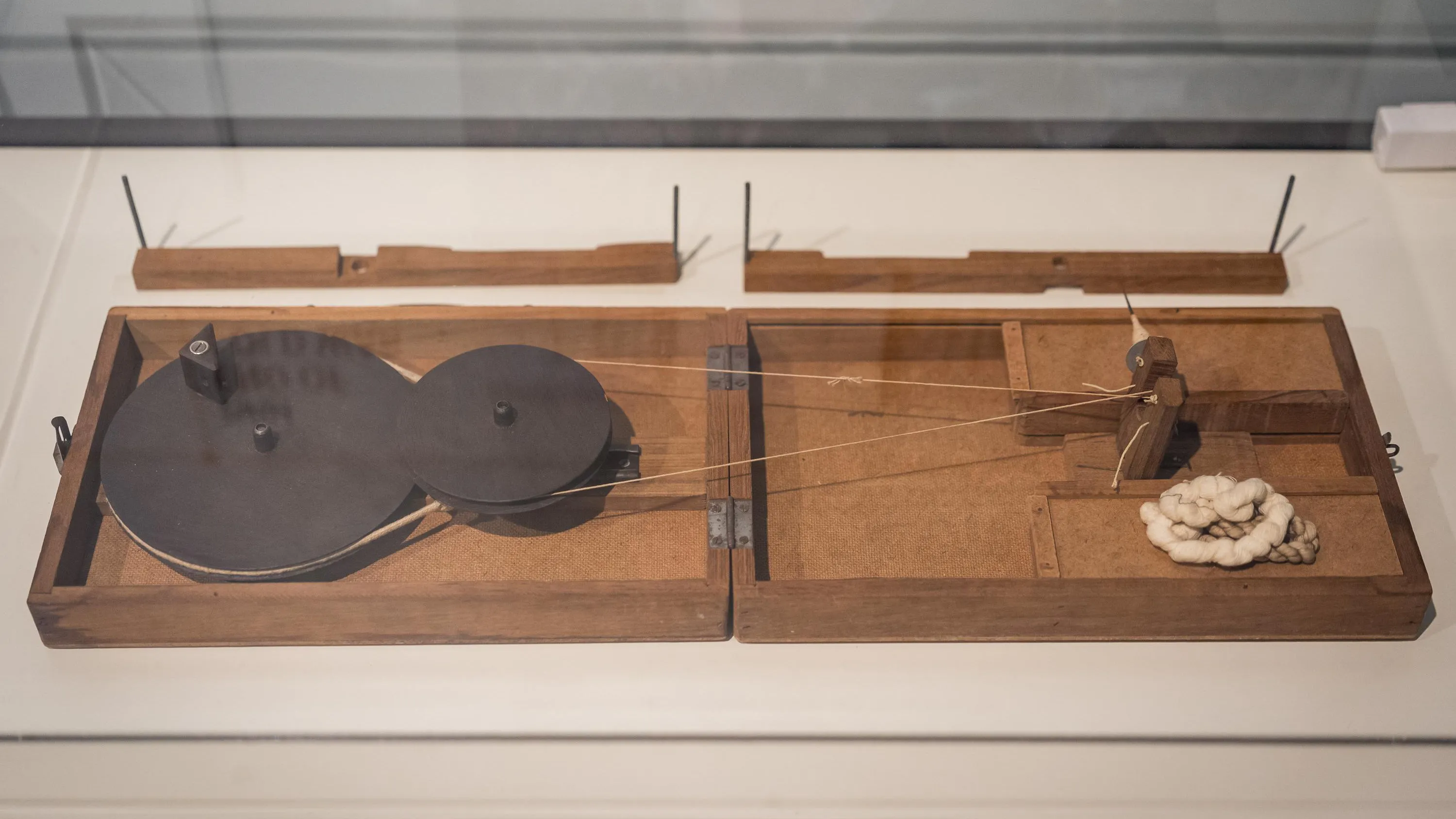 A flat wooden spinning wheel in a glass case