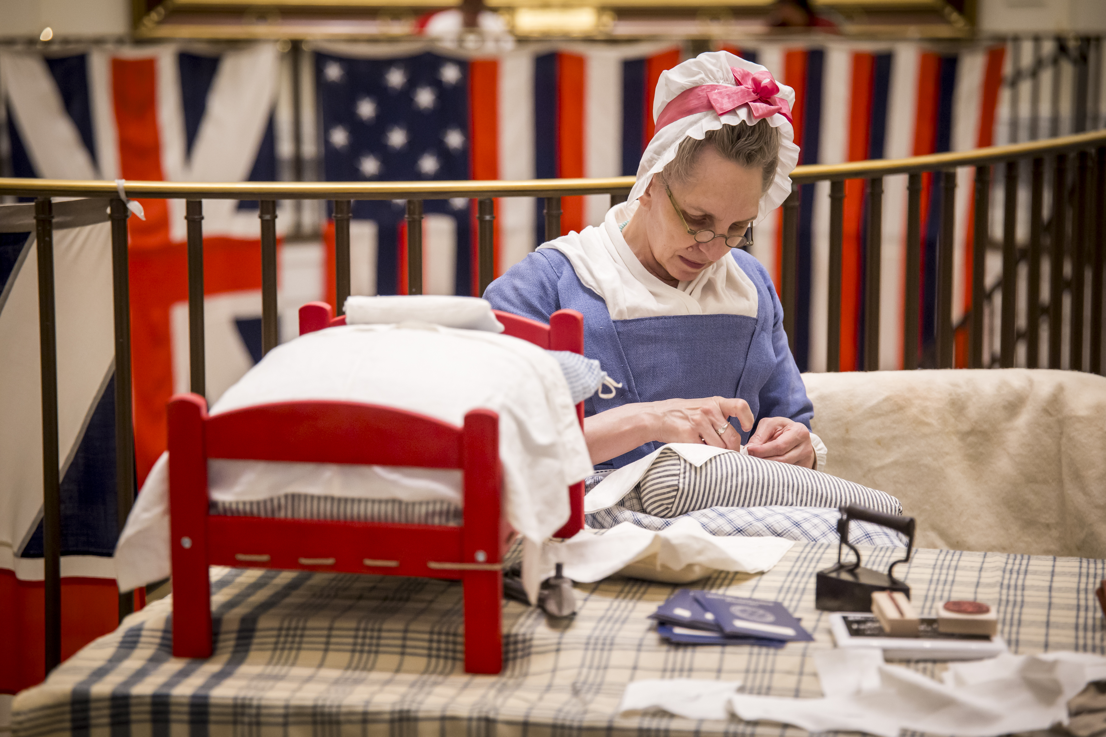 A costumed interpreter sews sitting in front of the True Colors project in the Museum