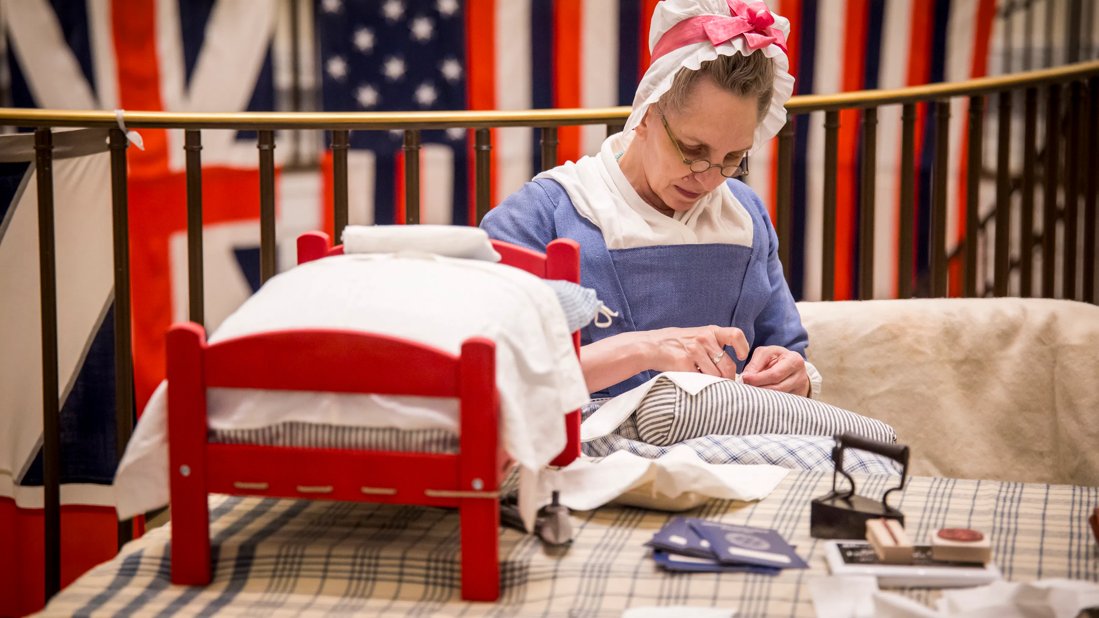 A costumed interpreter sews sitting in front of the True Colors project in the Museum
