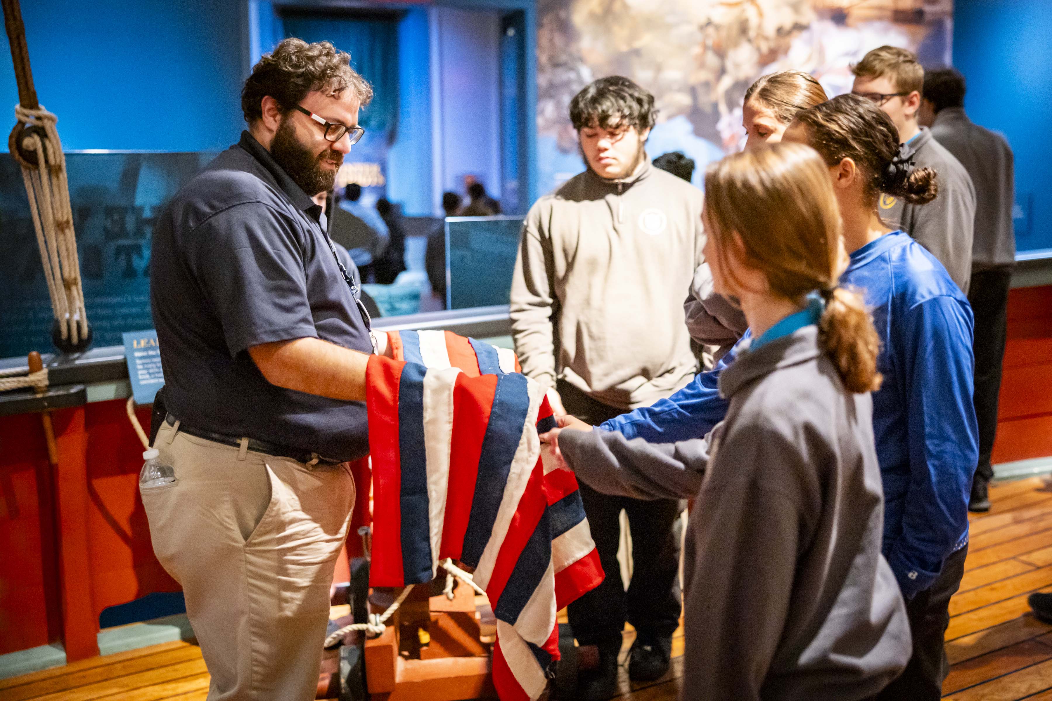 A Museum educator shows a group of school students a replica naval flag.