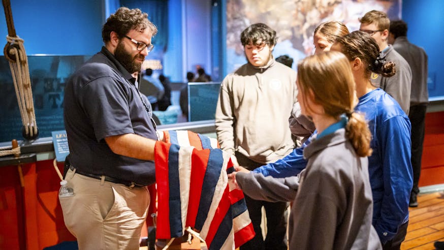 A Museum educator shows a group of school students a replica naval flag.