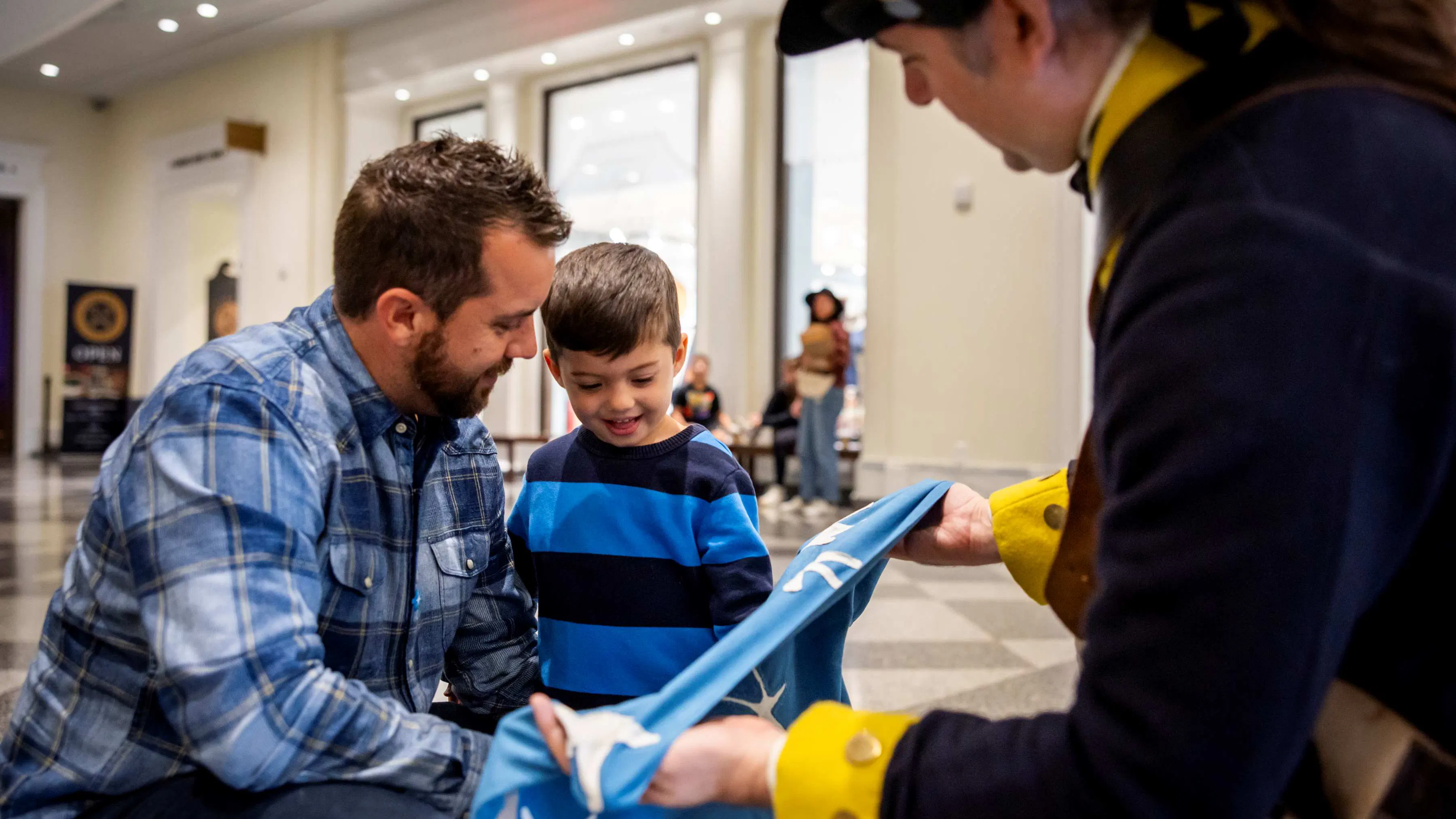 A man and a child interact with a replica flag held by a costumed interpreter