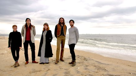 The five members of The Chivalrous Crickets musical group pose for a photo on a beach.