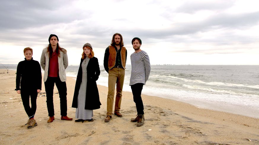 The five members of The Chivalrous Crickets musical group pose for a photo on a beach.