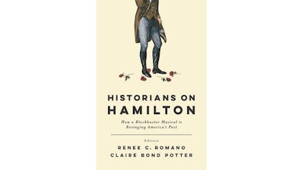 This image depicts the book cover of Historians on Hamilton: How a Blockbuster Musical is Restarting America’s Past edited by Rene Romano and Claire Potter. The book cover is tan, and the title of the book is written in black. There is a Revolutionary man, wearing black boots, blue pants, and a brown waist jacket. His left knee is bended, and the image cuts off around the man’s chest—his face is not visible. There are five roses scattered around his feet.