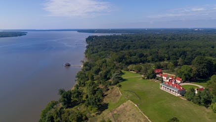 An aerial view of George Washington's Mount Vernon and greenery to the right and blue Potomac River to the left.