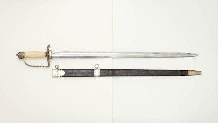 This image shows a British Officer's hanger. It is displayed below the sword on a white background. The hilt is a shade of gold while the sword is silver.