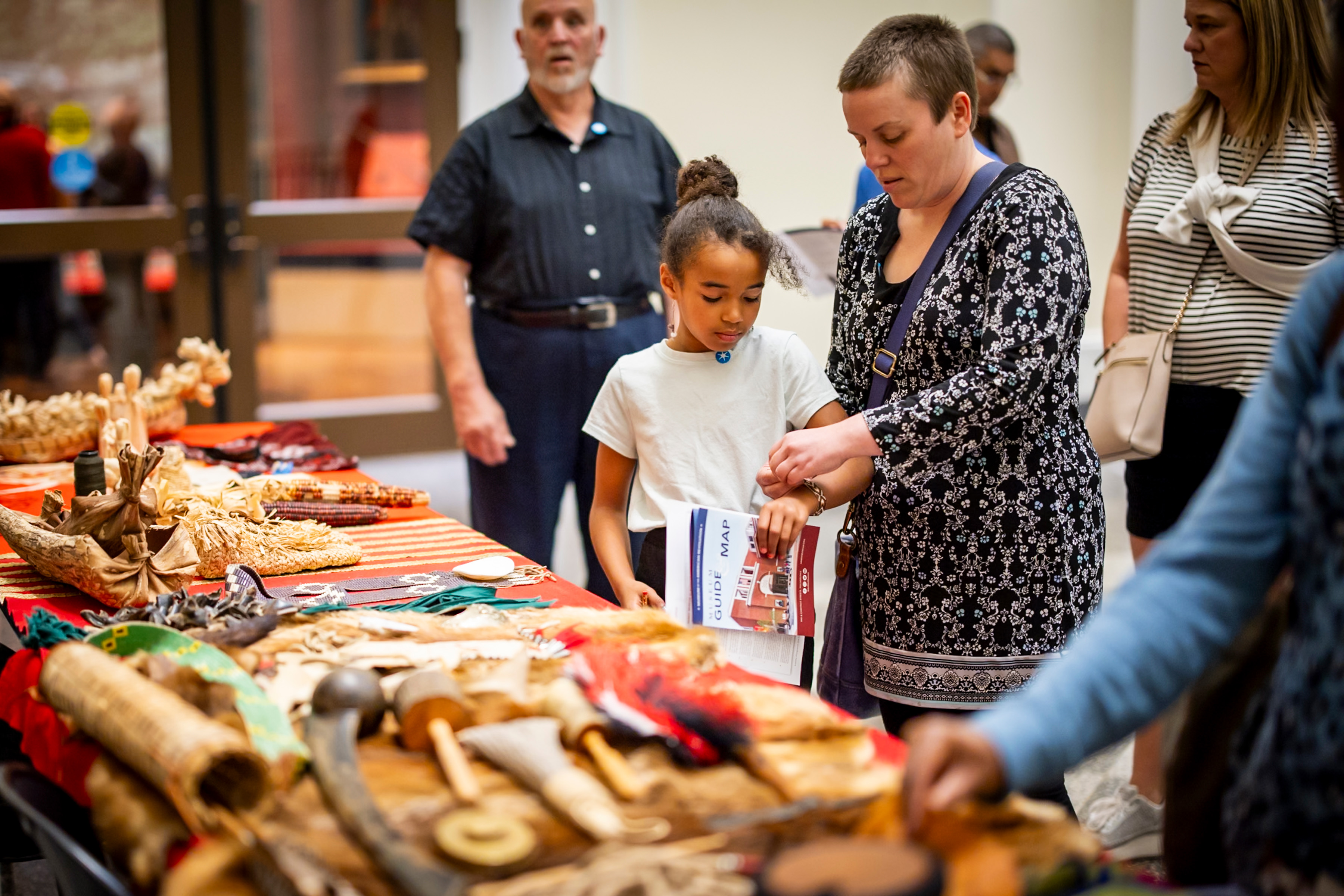 A woman and child stand in front of a table with Native American artifacts