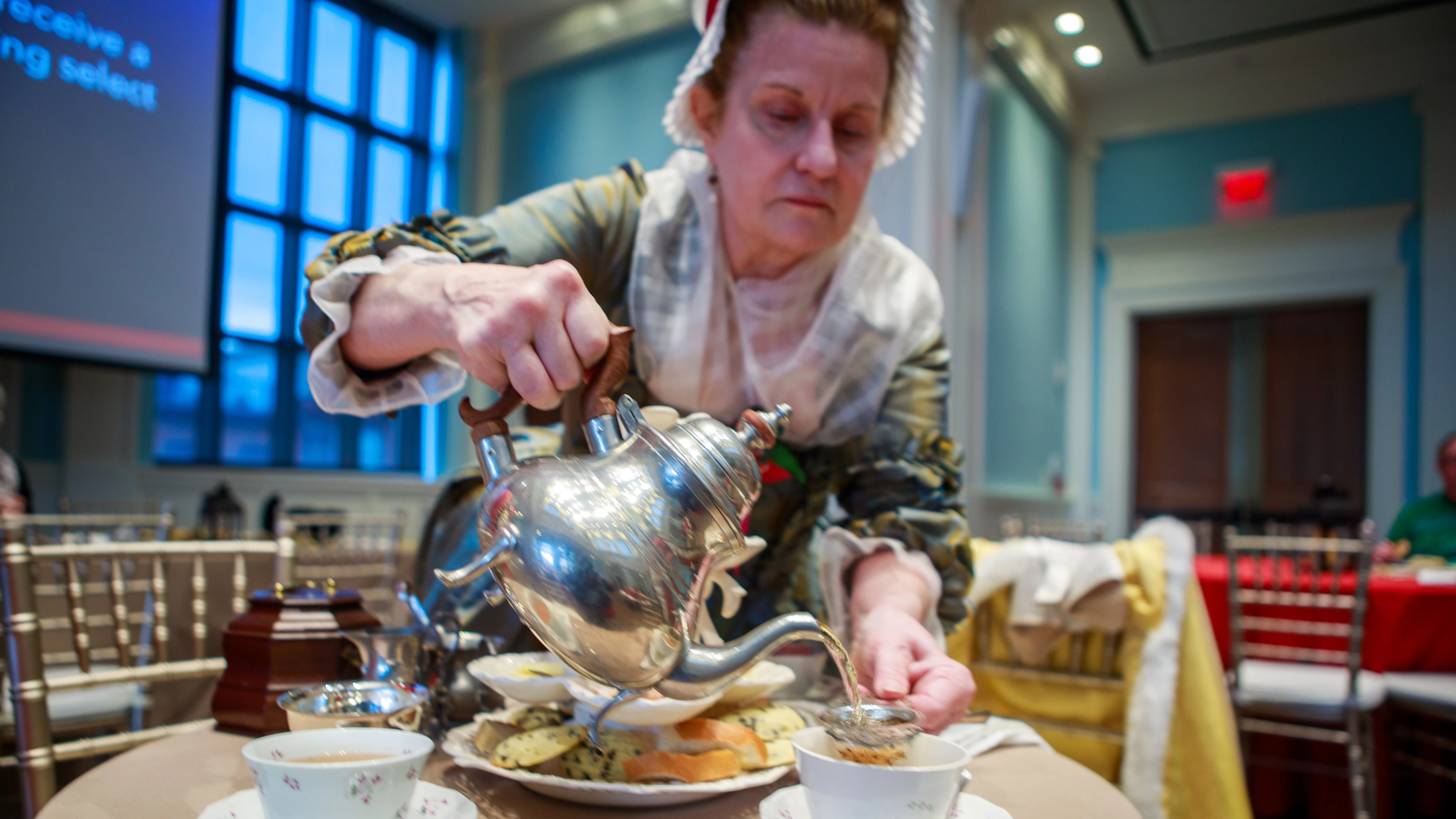A costumed interpreter pours tea from a silver teapot