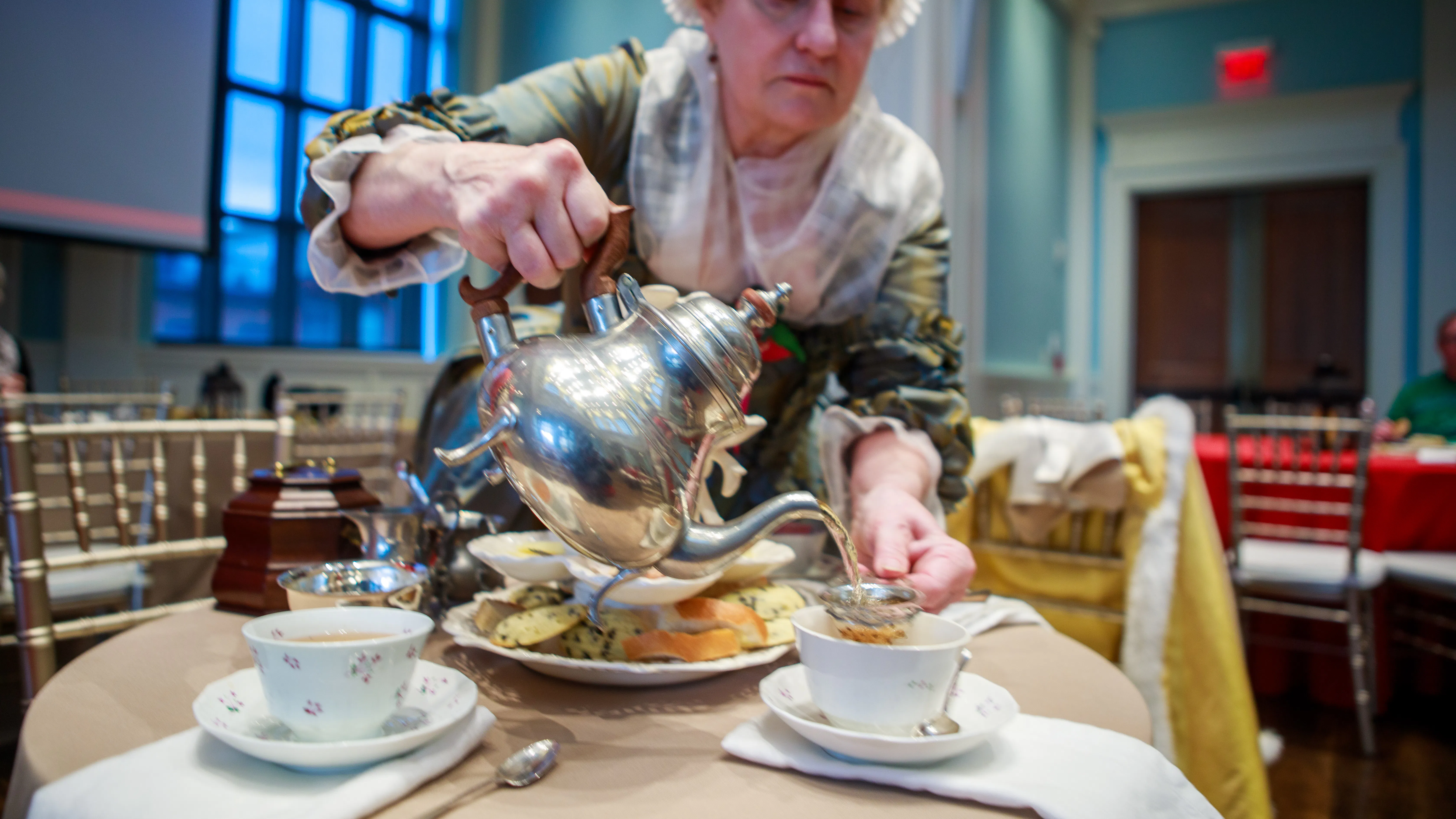 A costumed interpreter pours tea from a silver teapot