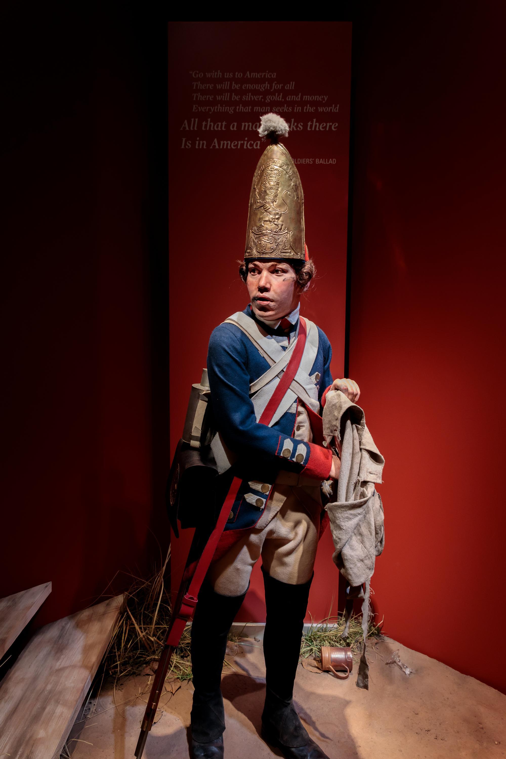 A lifesize figure of a soldier in 18th century clothes with a large gold helmet