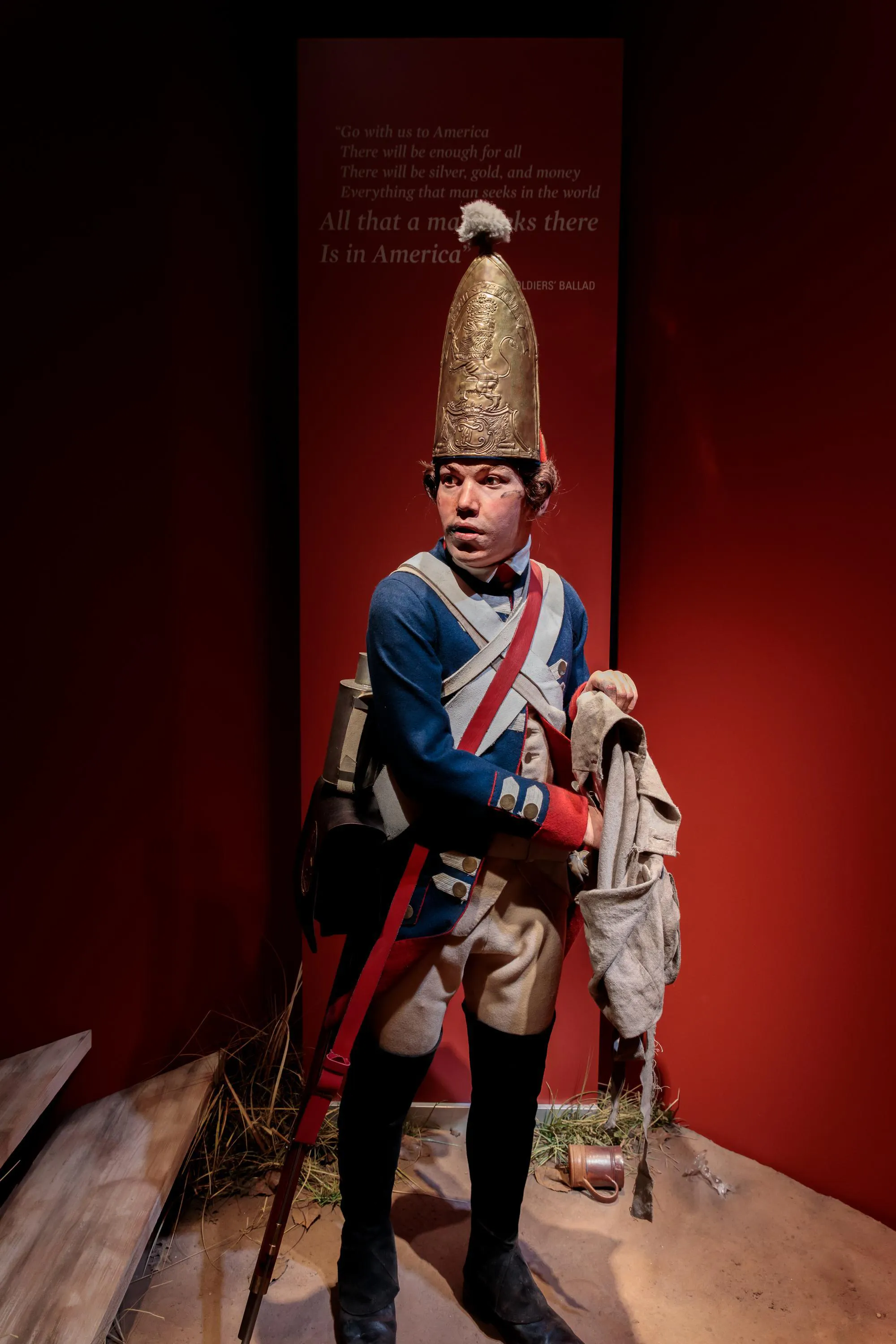 A lifesize figure of a soldier in 18th century clothes with a large gold helmet