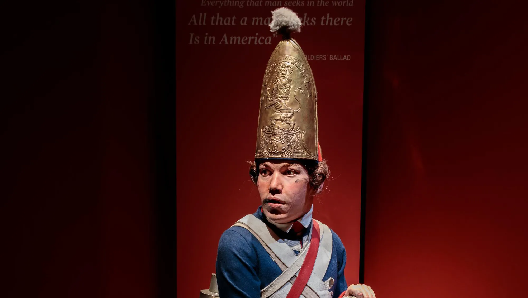 A lifesize figure of a soldier in 18th century clothes with a large gold helmet
