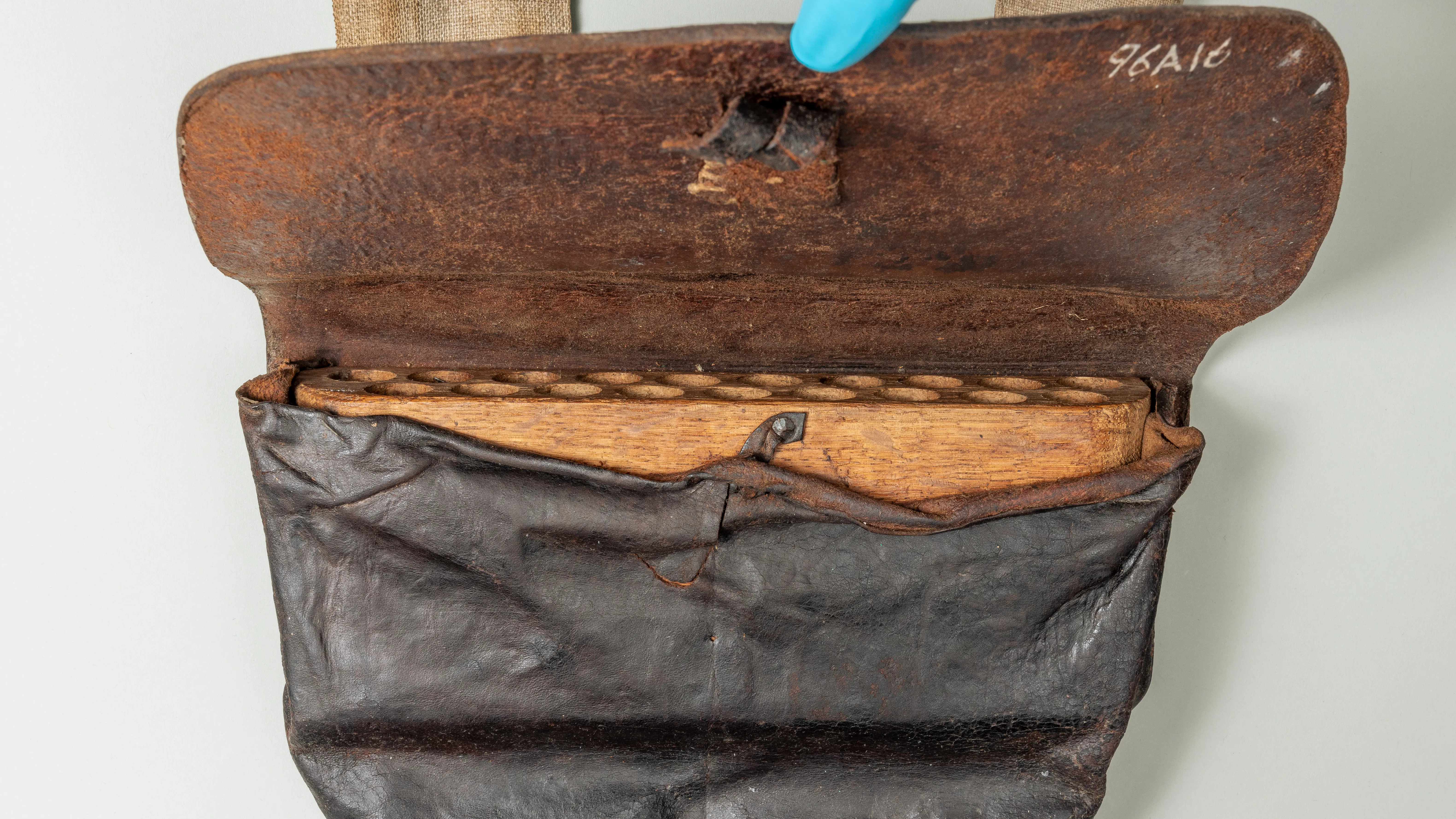 This image shows a curator holding the lid of the black leather cartridge box open to show the wooden interior with small holes drilled in it to hold the shots.