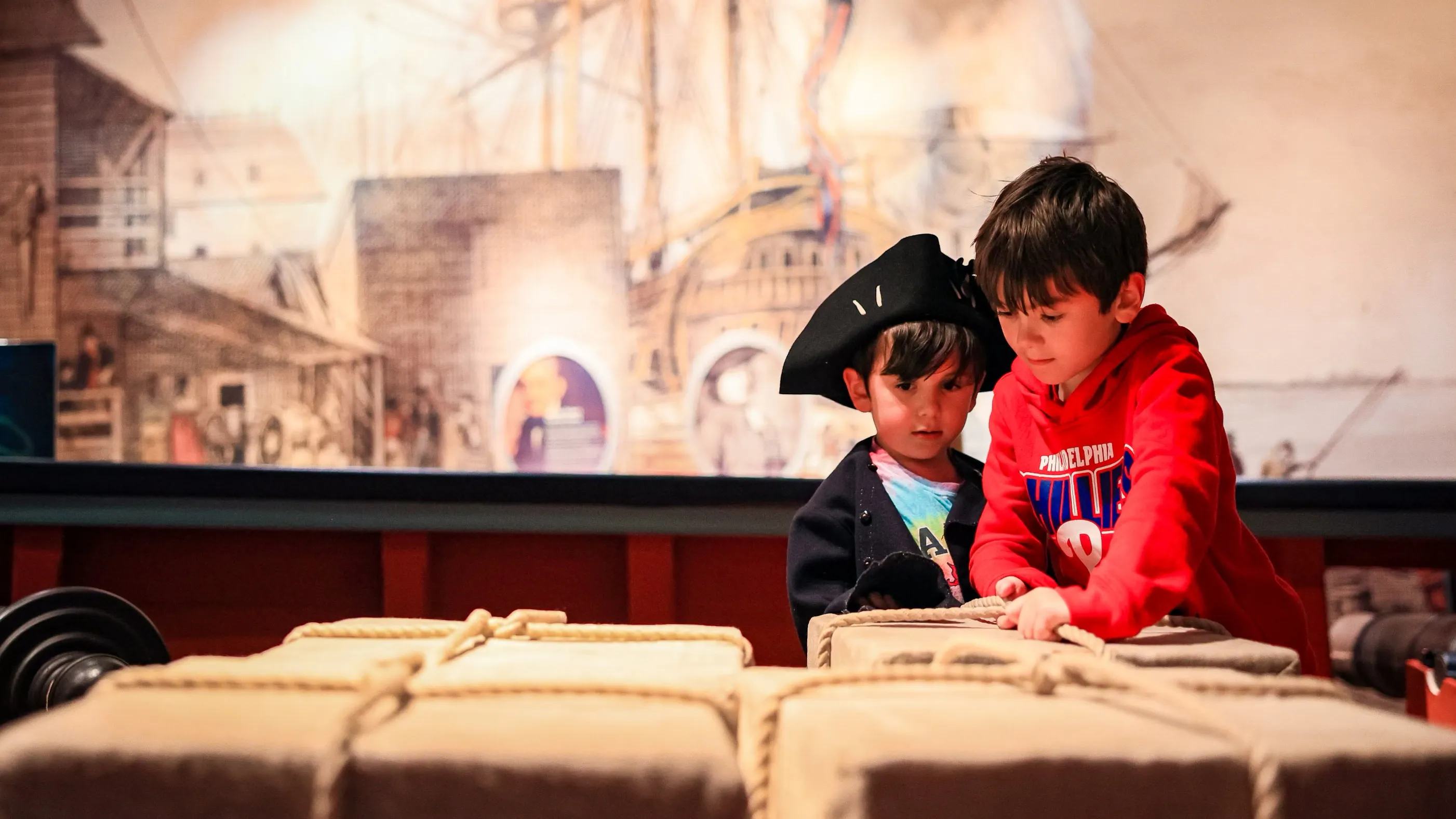 Two kids interact with replica cargo on replica privateer ship