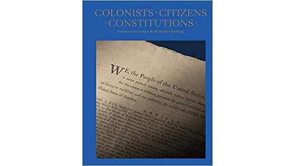 The image depicts Colonists Citizens Constitutions book cover by James Hrdlicka. It is a blue cover with a photo of the first few lines of the constitution. “We, the people of the United States,” is a visible.