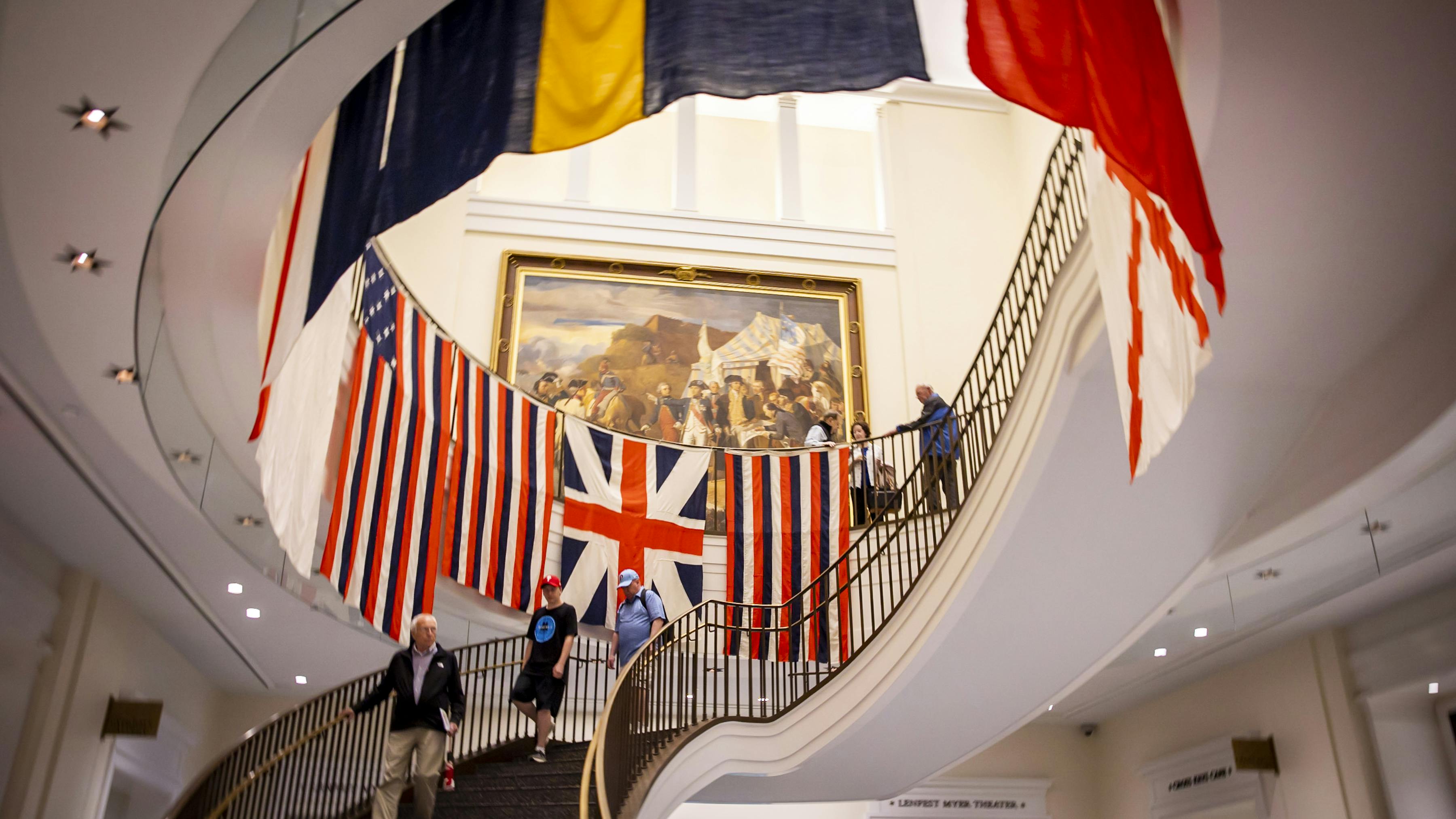 Image looking up the grand staircase at the replica flags created for the True Colours Flag Project around the railings with vistors walking up and down the stairs.