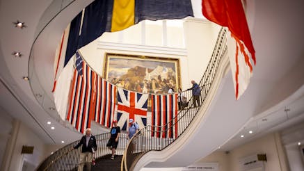 Image looking up the grand staircase at the replica flags created for the True Colours Flag Project around the railings with vistors walking up and down the stairs.