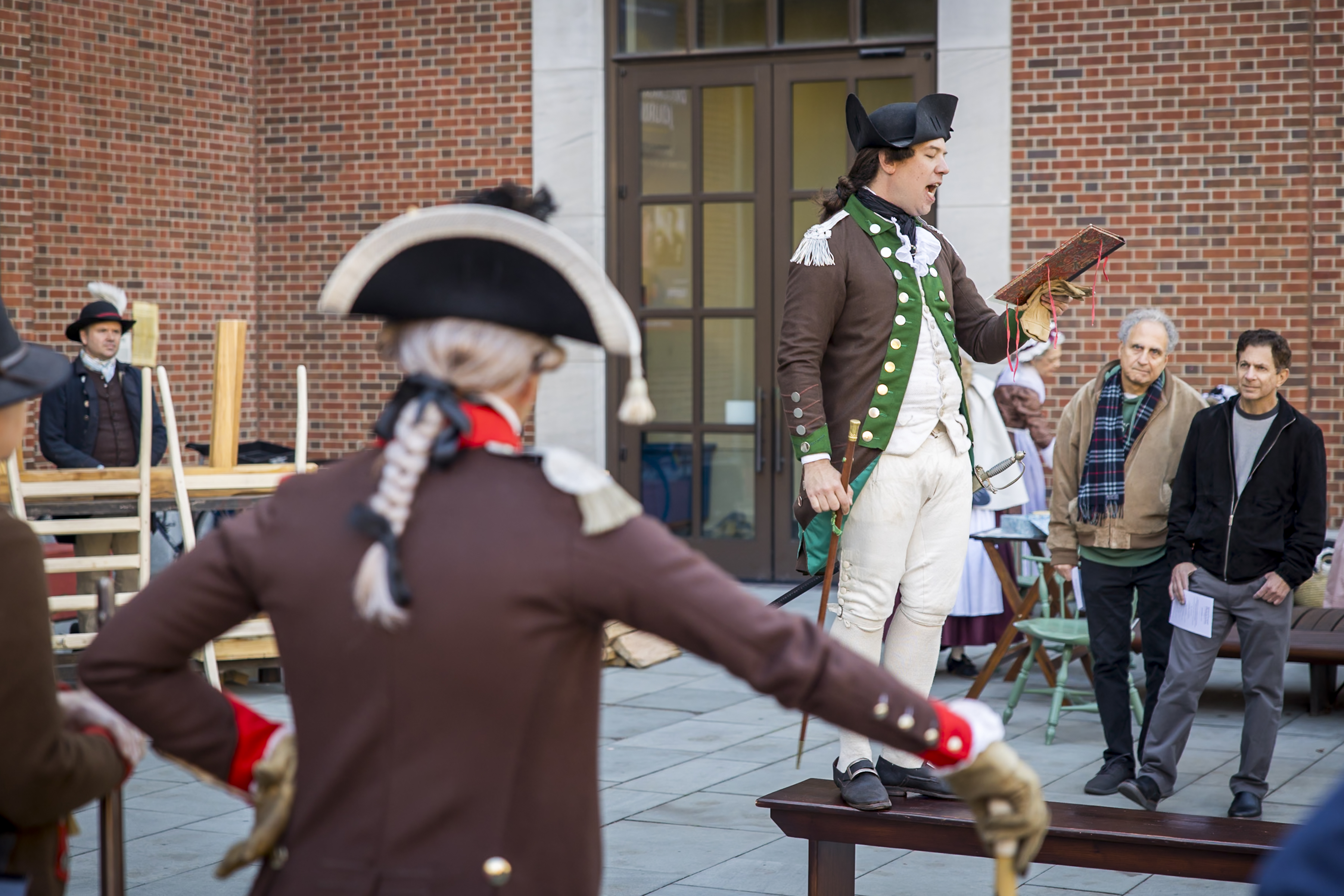 A costumed interpreter reads from a book while another watches