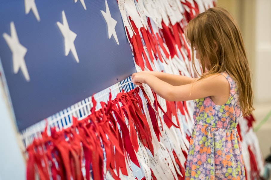 A young visitor ties a ribbon to our ribbon flag installation asking guests how they will be the revolution