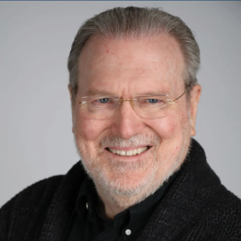 A white man with gray hair and a gray beard wearing glasses and a black shirt