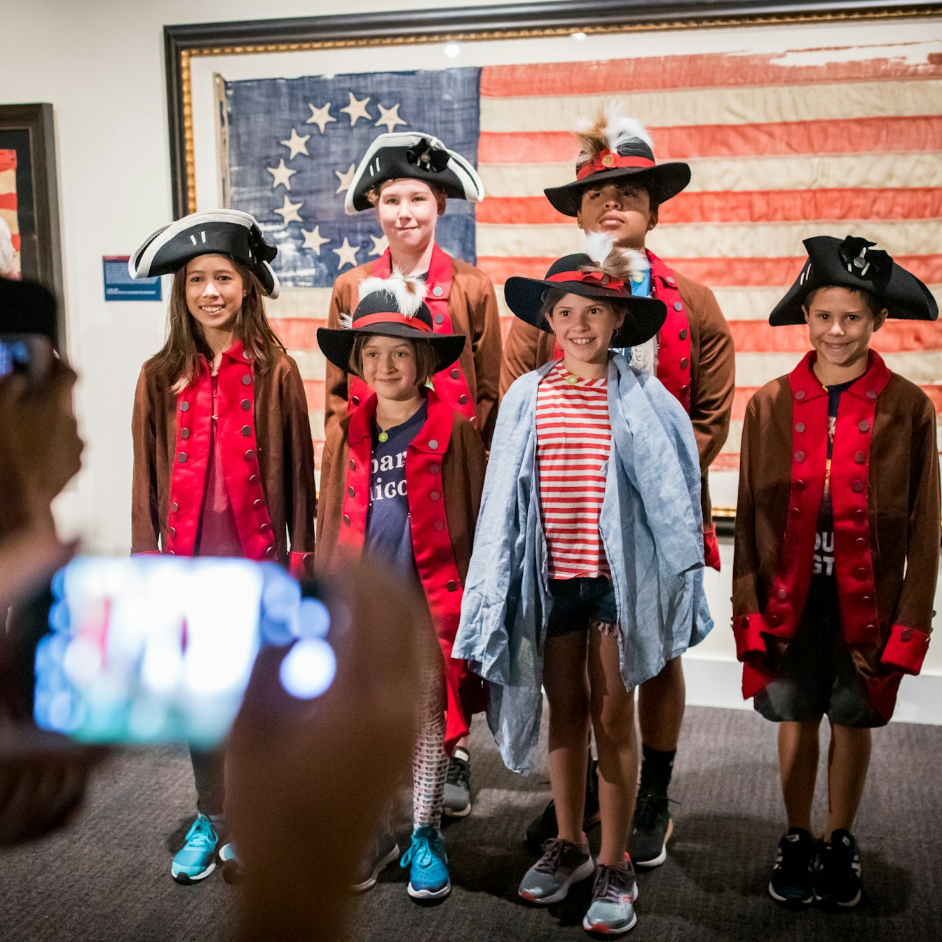 Six adolescents, wearing Revolutionary-era costumes, pose for a picture in front of a 13-star flag, which was part of the Museum's summer 2019 exhibition, A New Constellation.