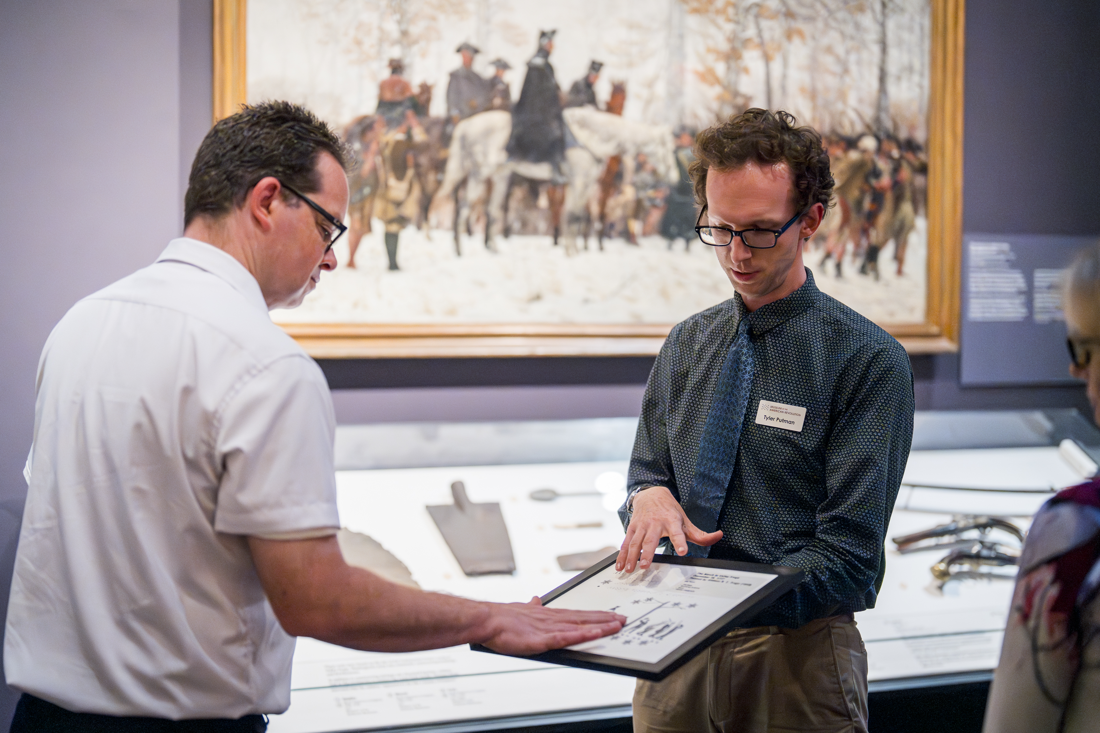 Museum educator shows object to man in white shirt and glasses
