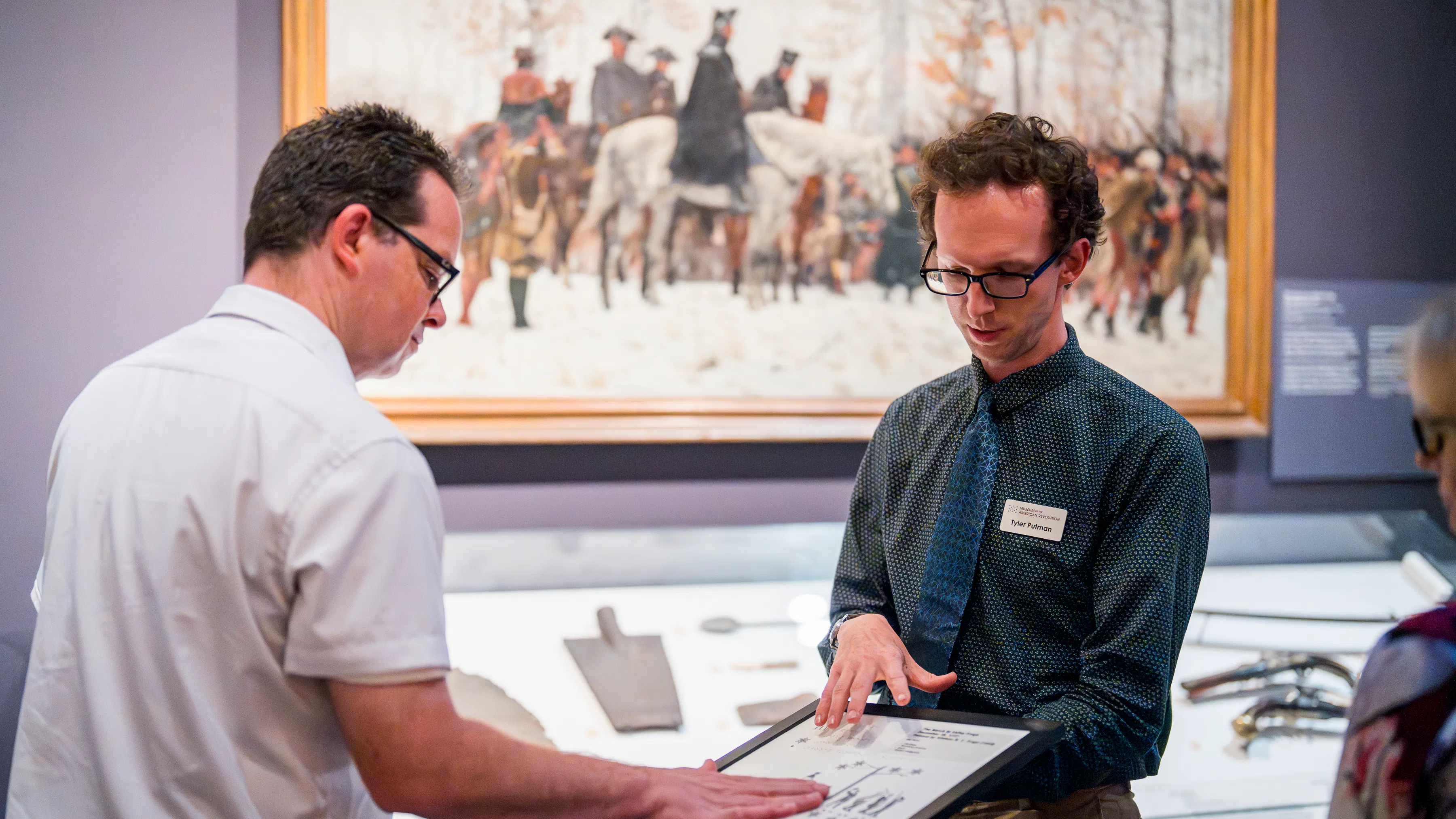 Museum educator shows object to man in white shirt and glasses