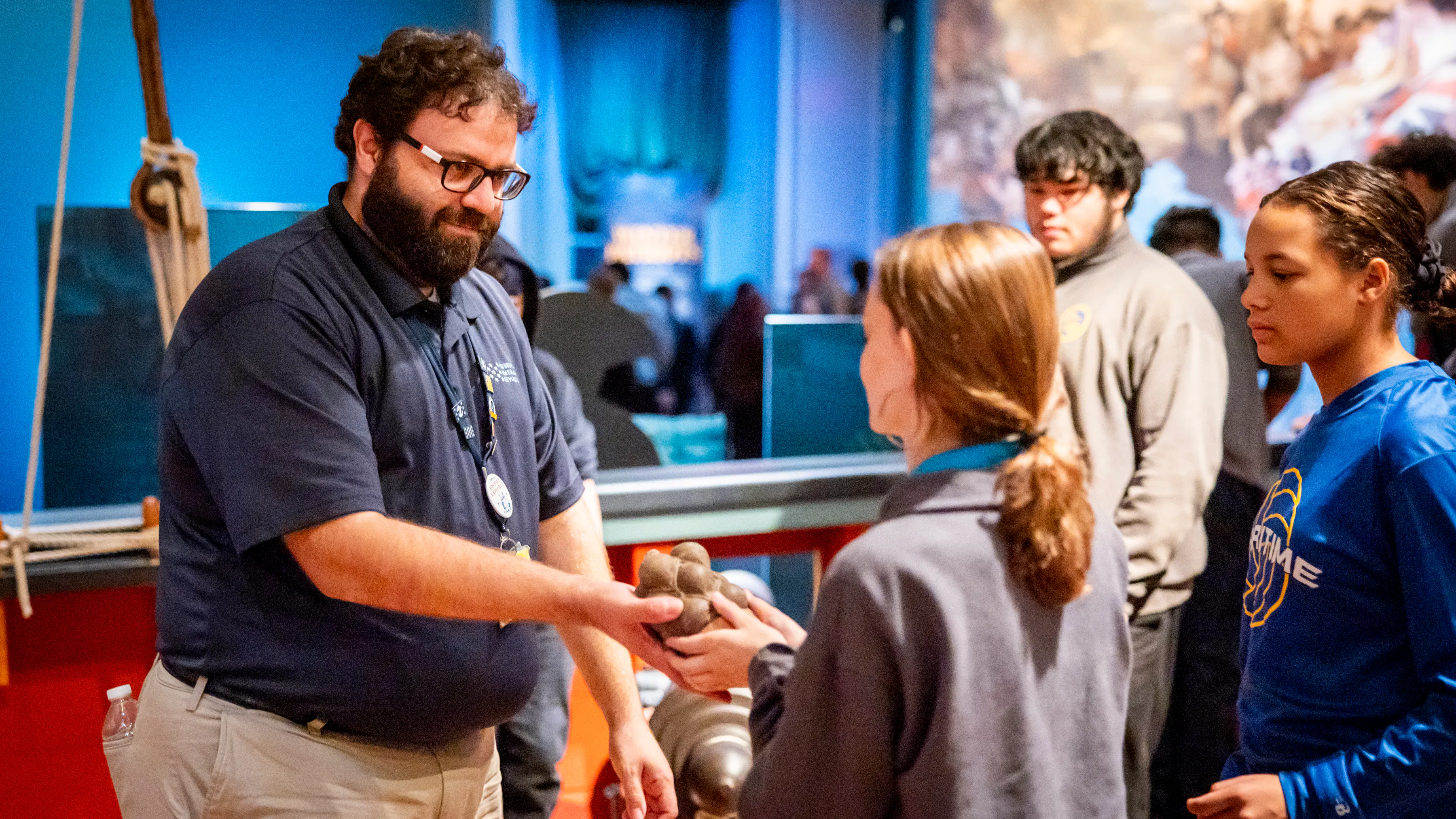 Museum educator wearing navy blue shirt holds grapeshot for young student