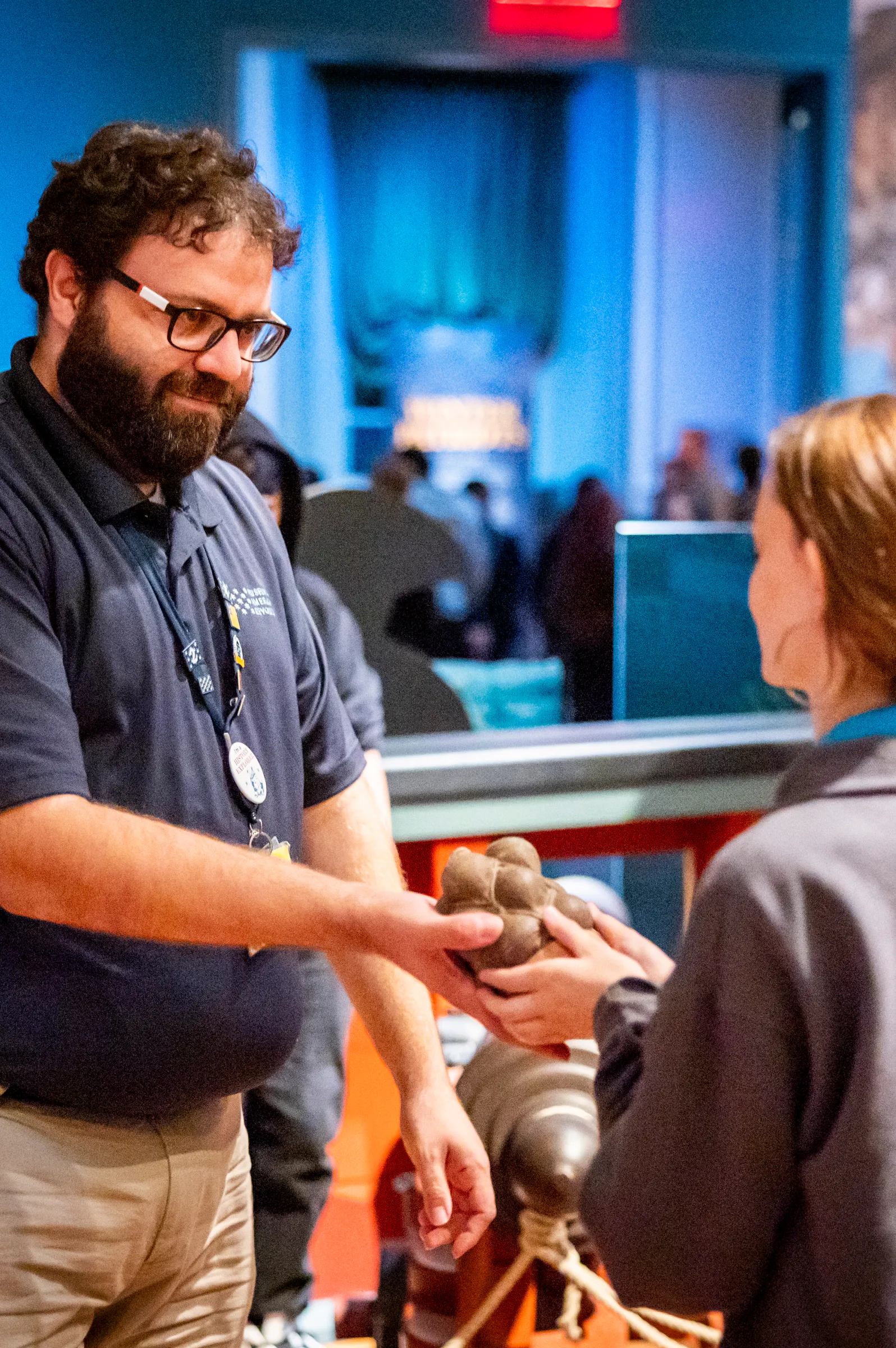 Museum educator wearing navy blue shirt holds grapeshot for young student